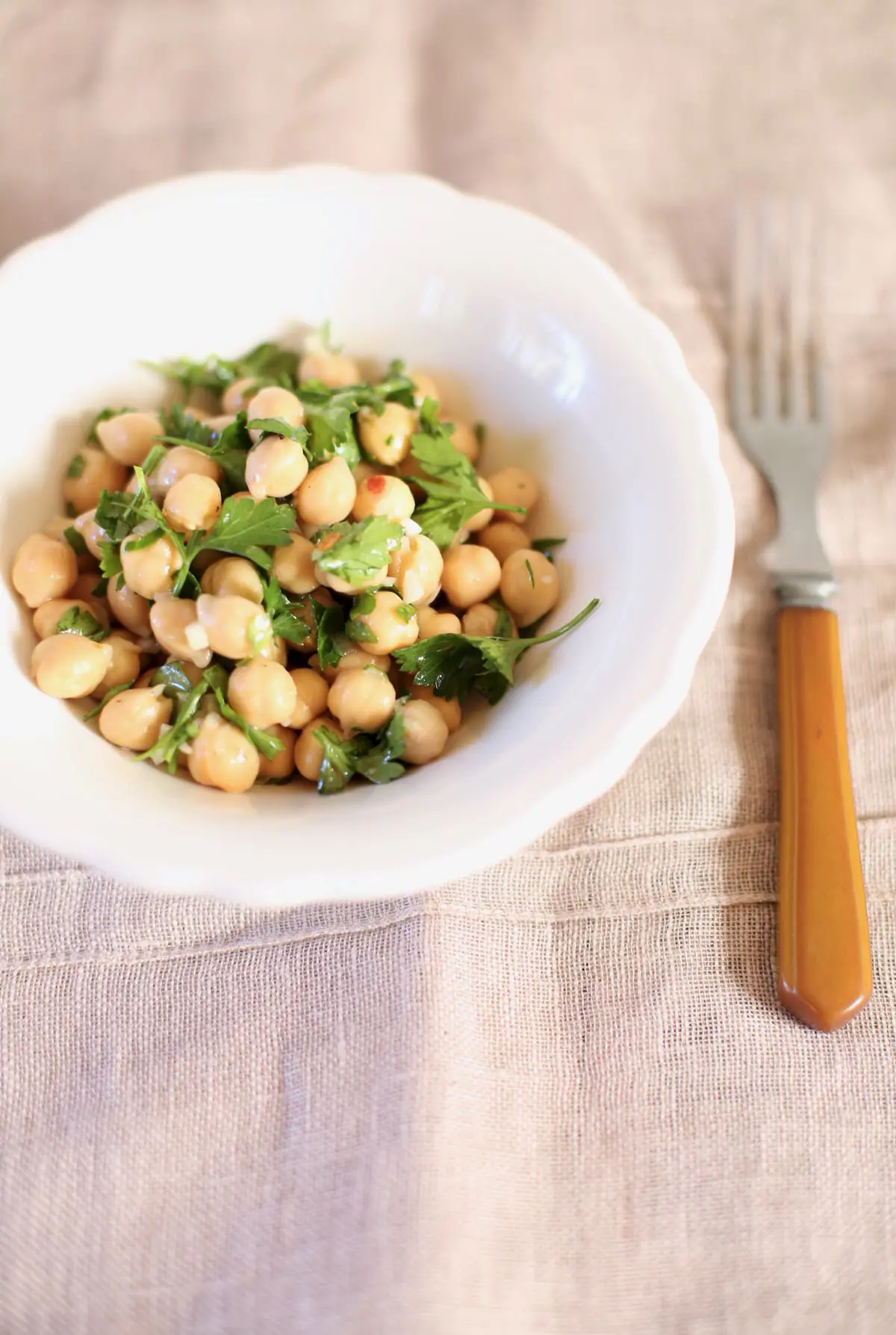 chickpea salad in a white bowl with a brown fork