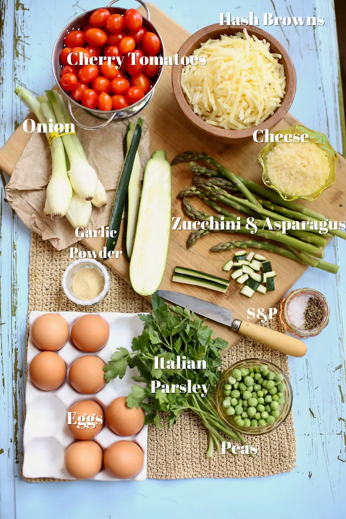 a variety of ingredients for a frittata on a blue table with text 