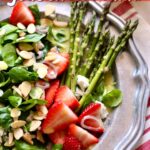 a silver plate with a salad of strawberries, goat cheese, almonds and asparagus on it.