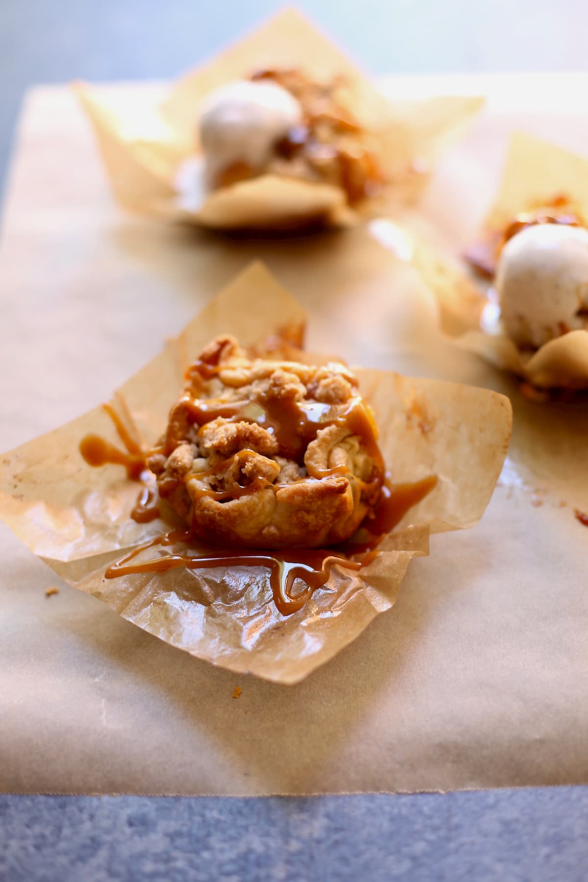 one muffin tin apple pie on a parchment paper square with caramel 