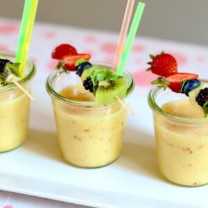 three smoothies with fruit on a table.