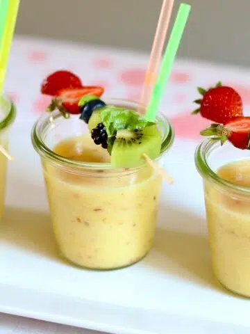 three smoothies with fruit on a table.
