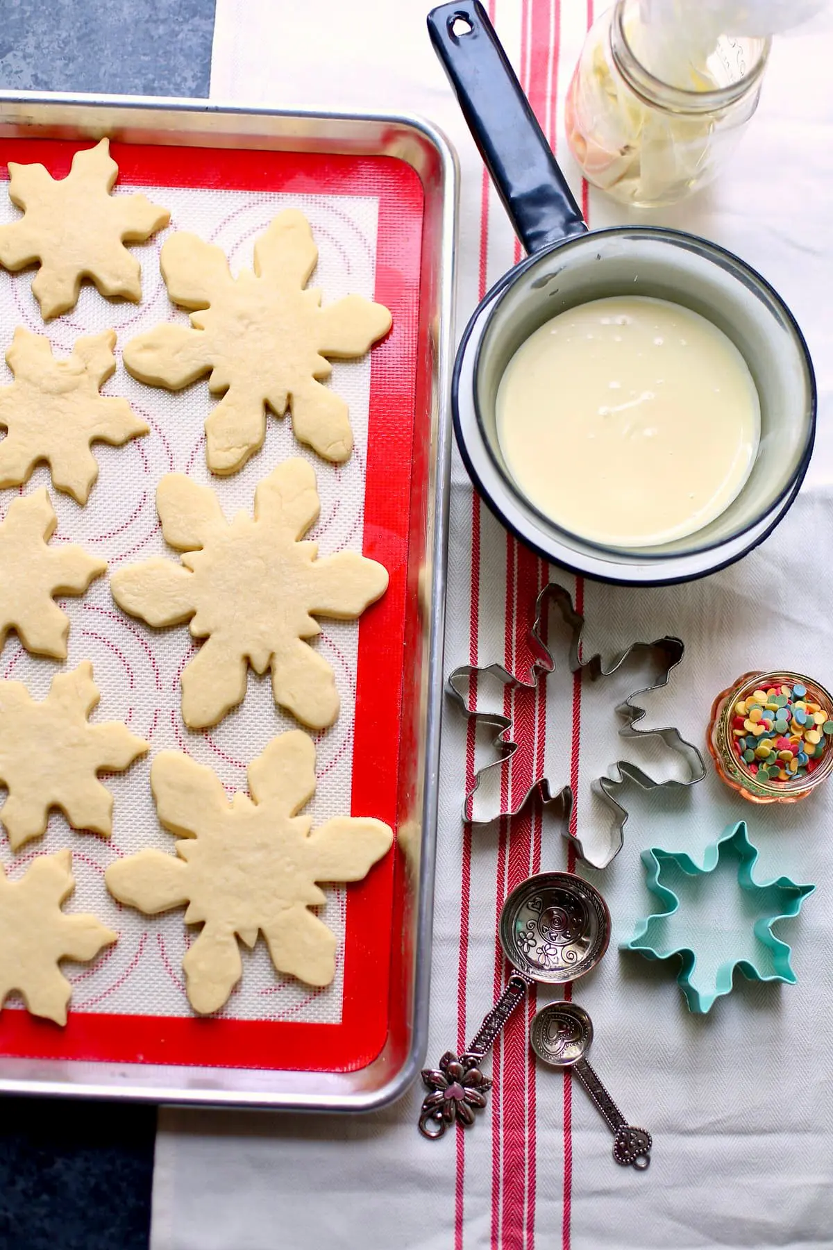cooked cookies with frosting and snowflake cut outs on a baking sheet