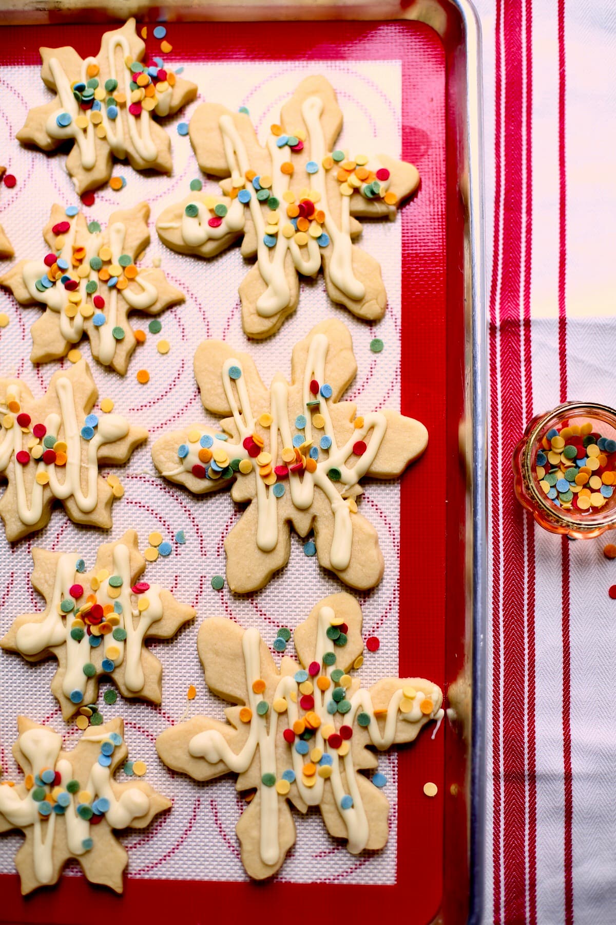 Finished snowflake cookies frosted with sprinkles on a baking sheet