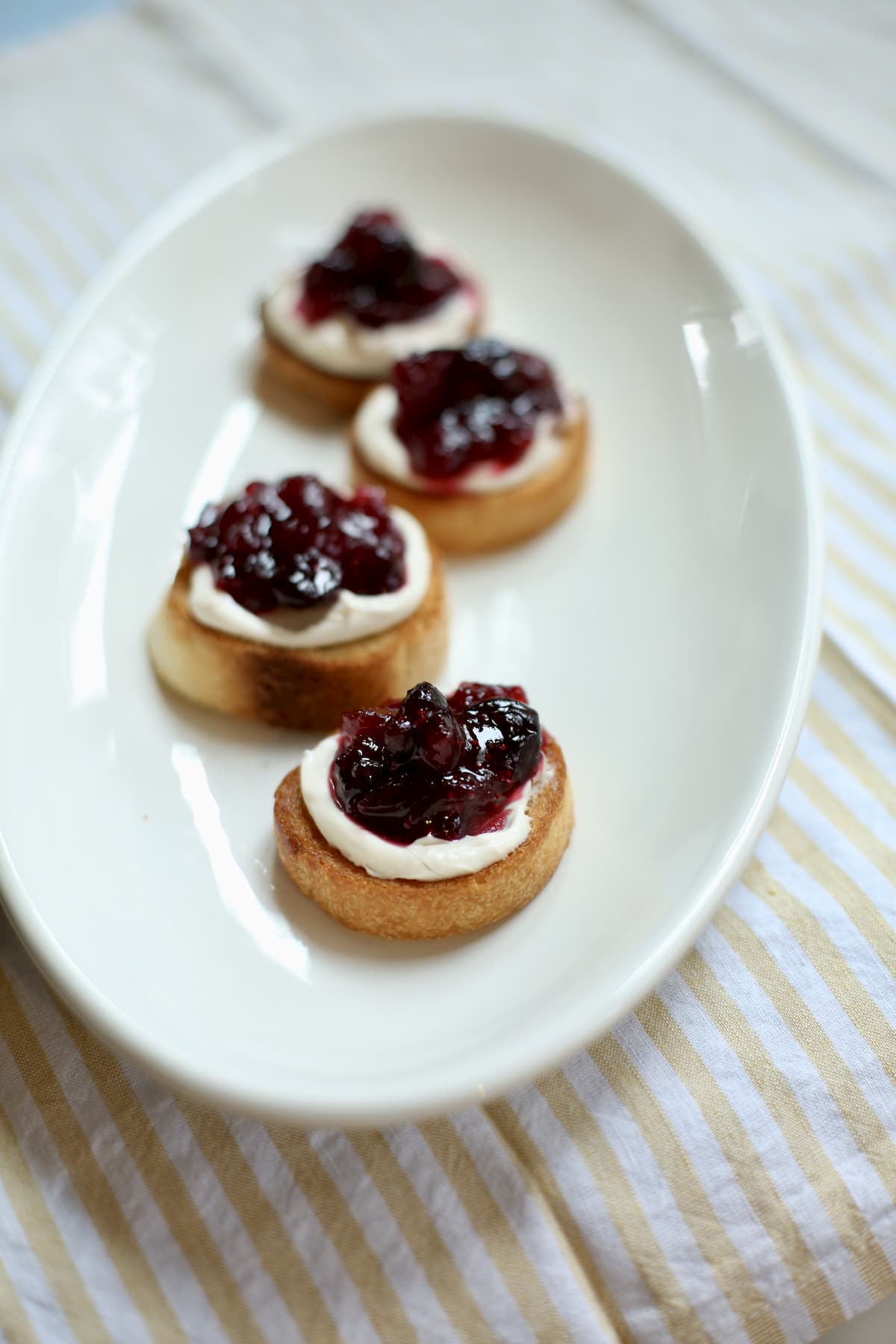 four ungarnished appetizers on a white dish with cheese and cranberry sauce on top