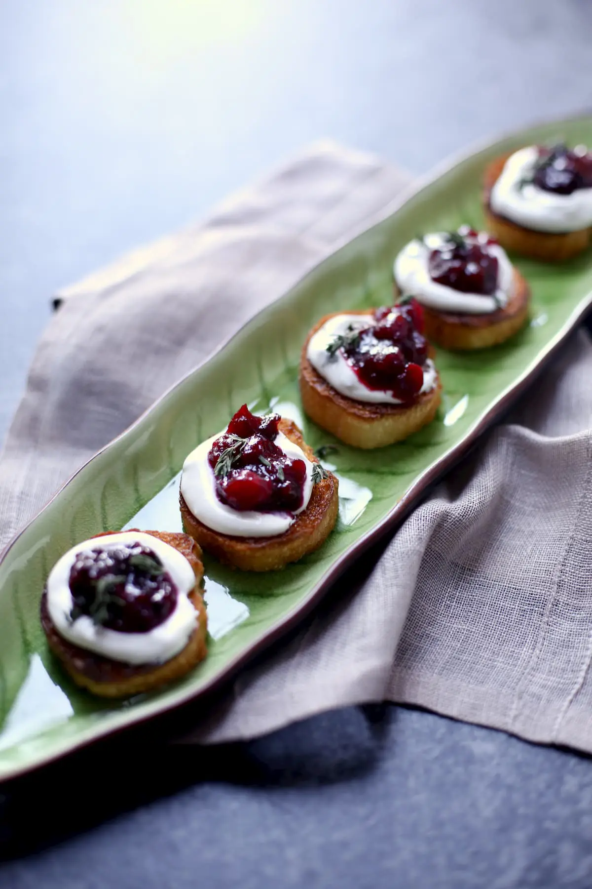 four appetizer toasts on a long green serving platter on a tablecloth