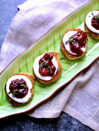 close up photo of several toast appetixers with cranberry and cheese on a long thin green serving tray