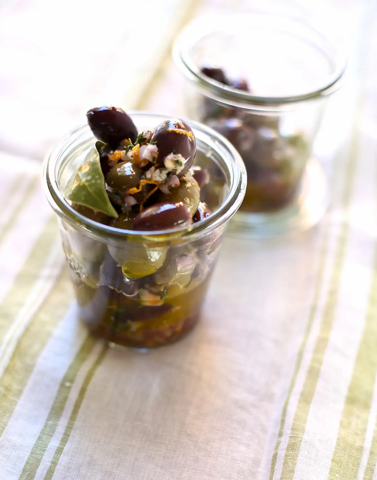 a weck jar with olives oil and bay leaf on a striped tablecloth