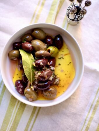 a bowl of olives with bay leaf and olive oil in a white bowl on a table