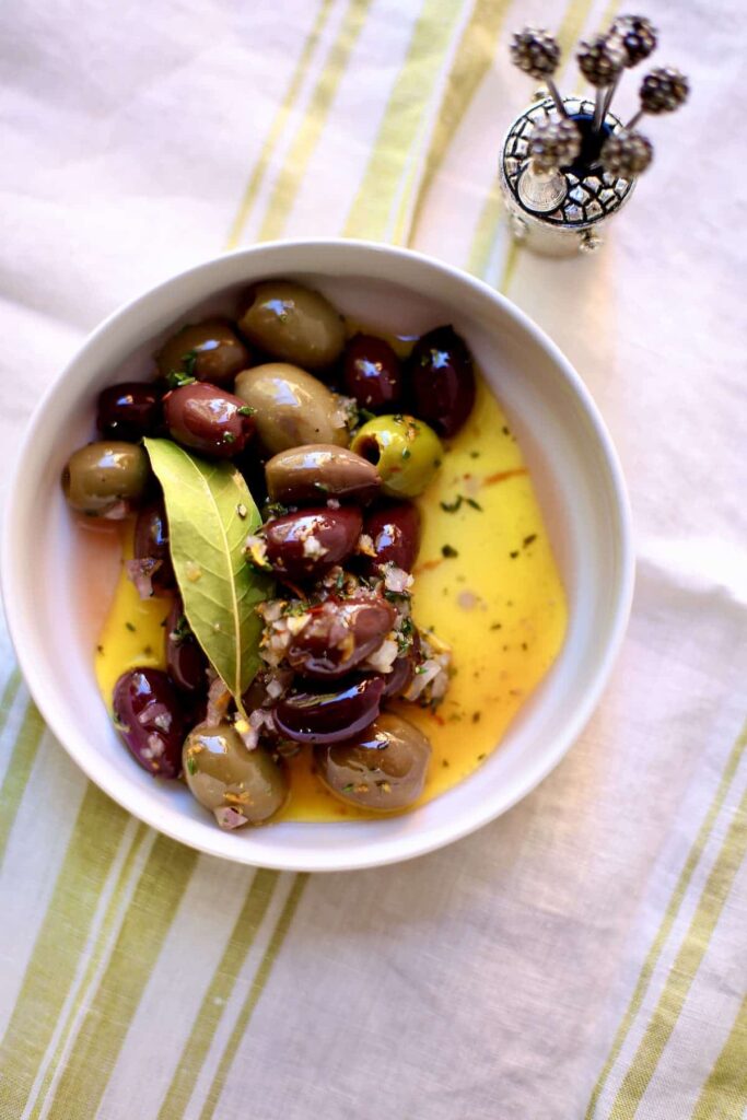 a bowl of olives with bay leaf and olive oil in a white bowl on a table