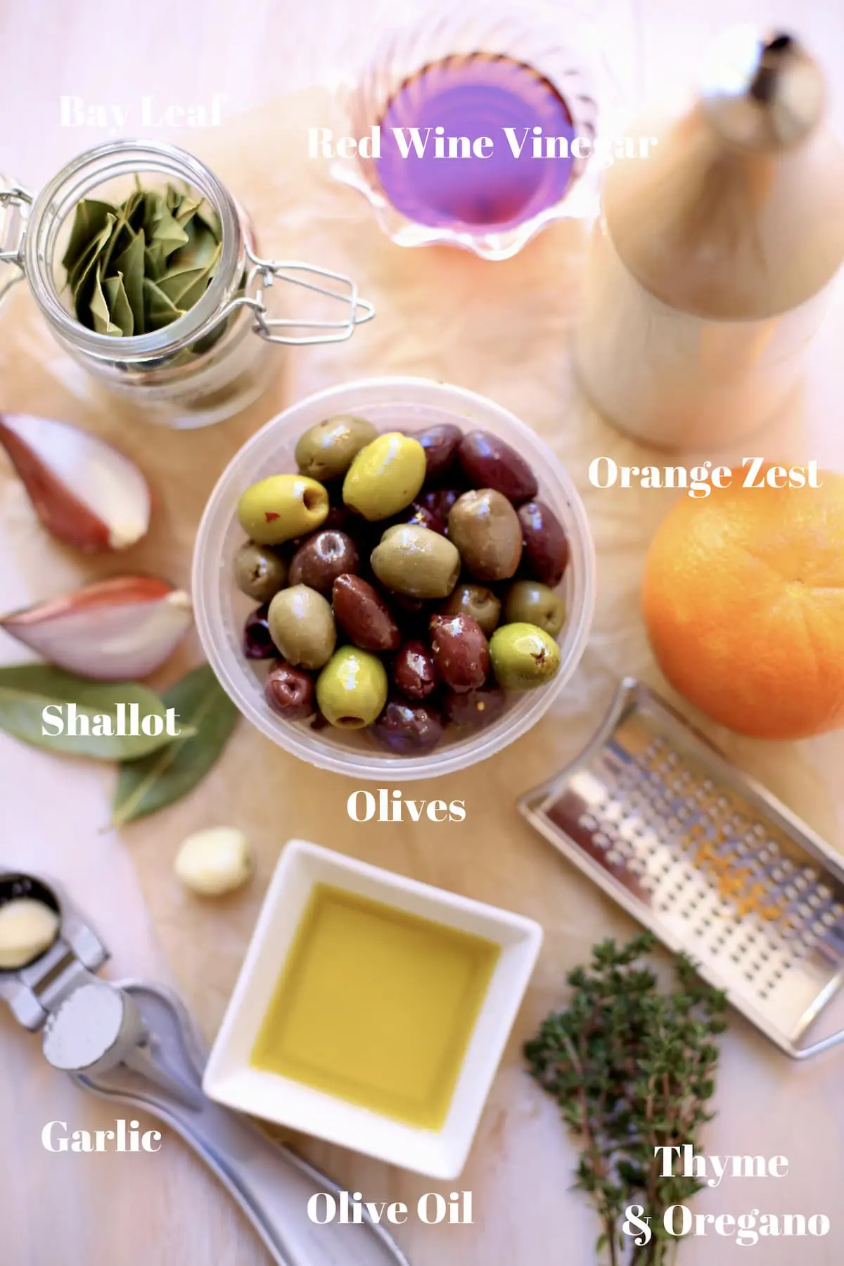 olives, orange, bay leaves, olive oil, shallot, thyme on on table with text underneath 