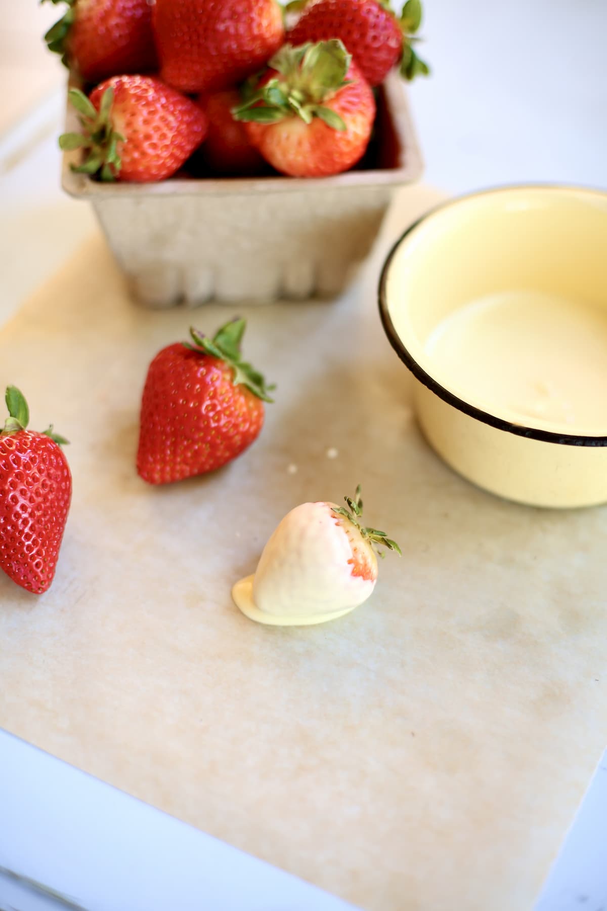 a set up of white chocolate and strawberries, one after being dunked and parchment paper