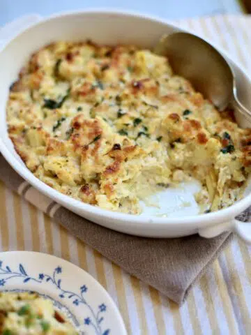 a white casserole dish of artichoke dip with a scoop of it removed
