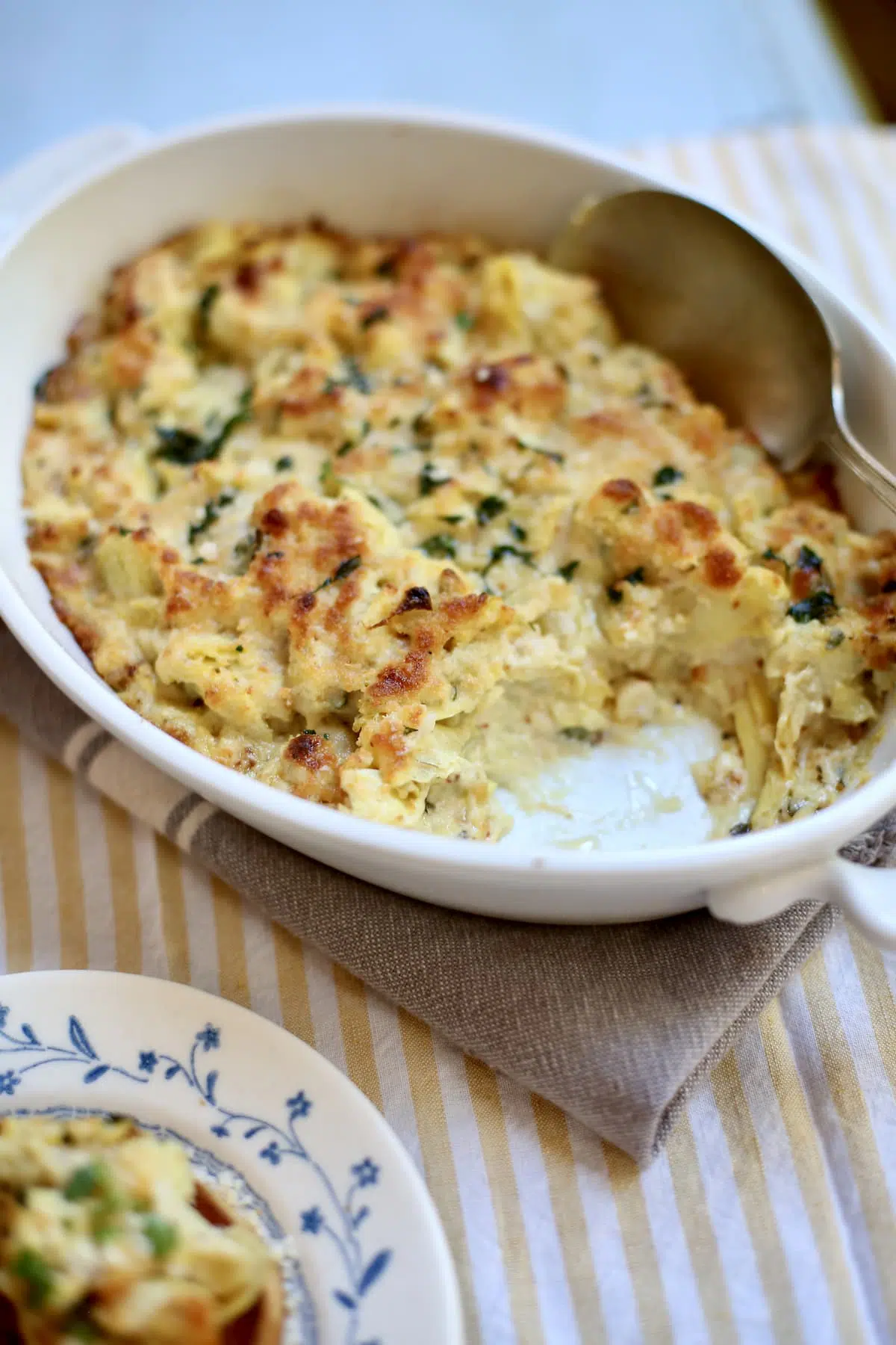 a white casserole dish of artichoke dip with a scoop of it removed