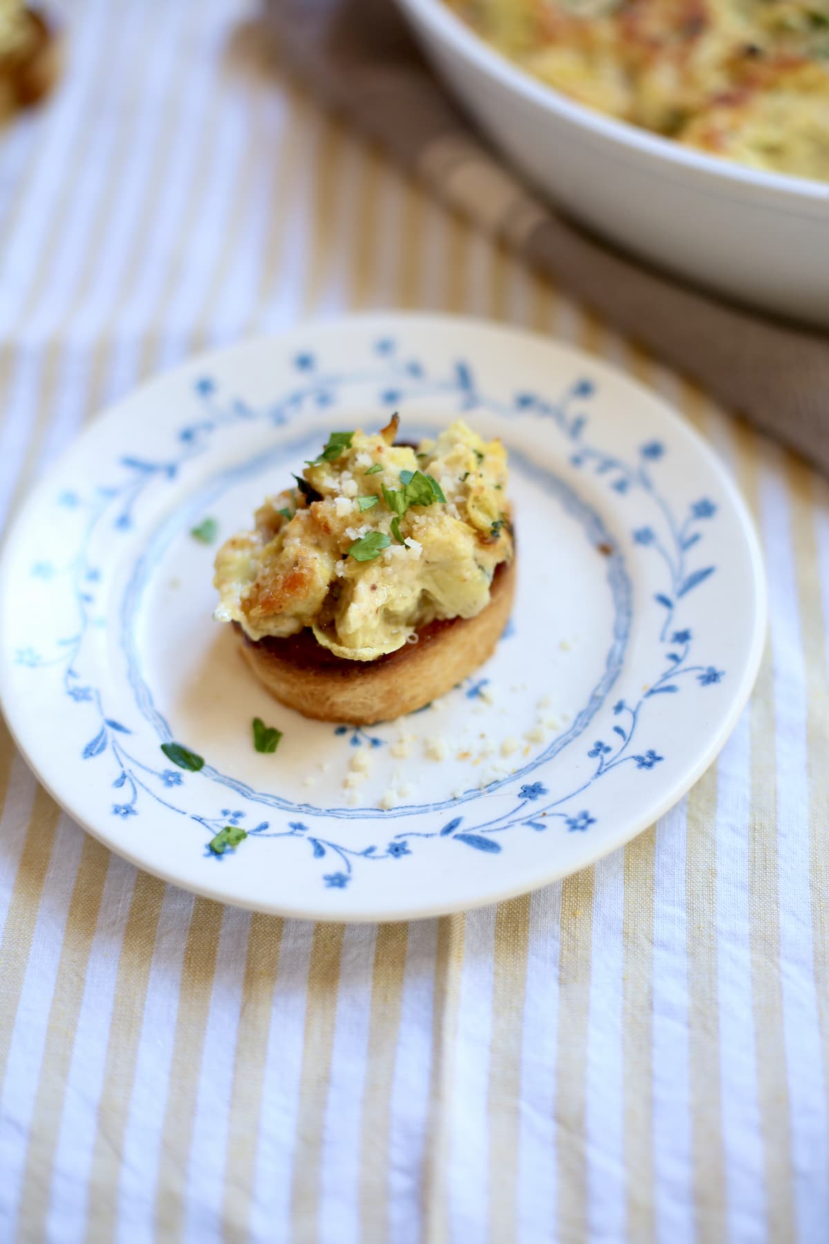 one piece of toasted bread with lemon artichoke dip on it on a blue flowered plate