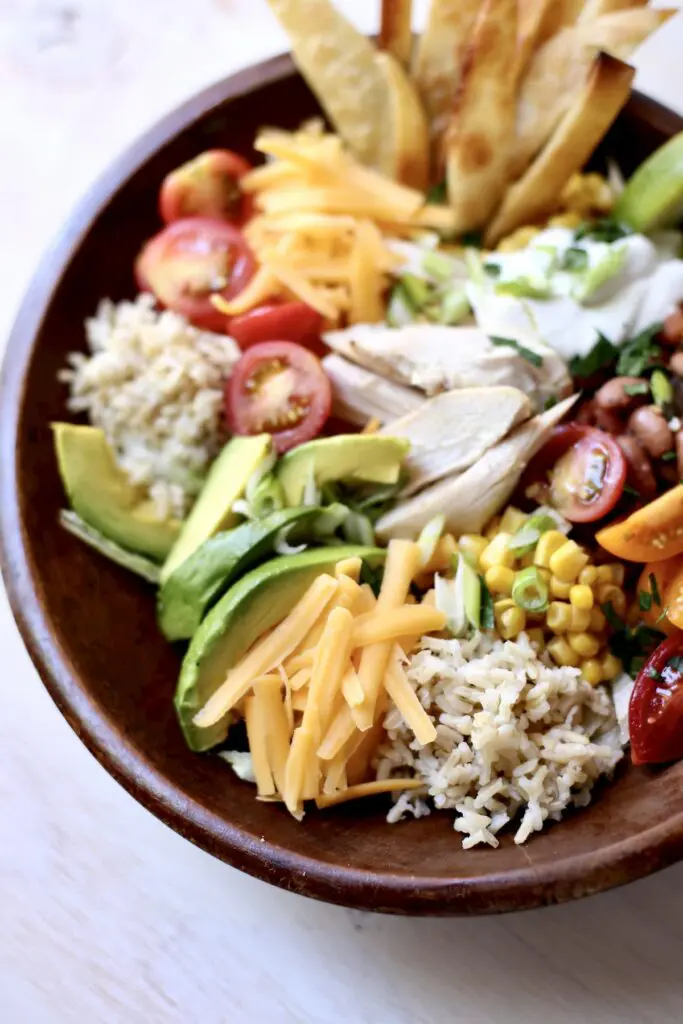 Close up photo of a bowl with cheese rice chicken tomatoes avaocado and corn