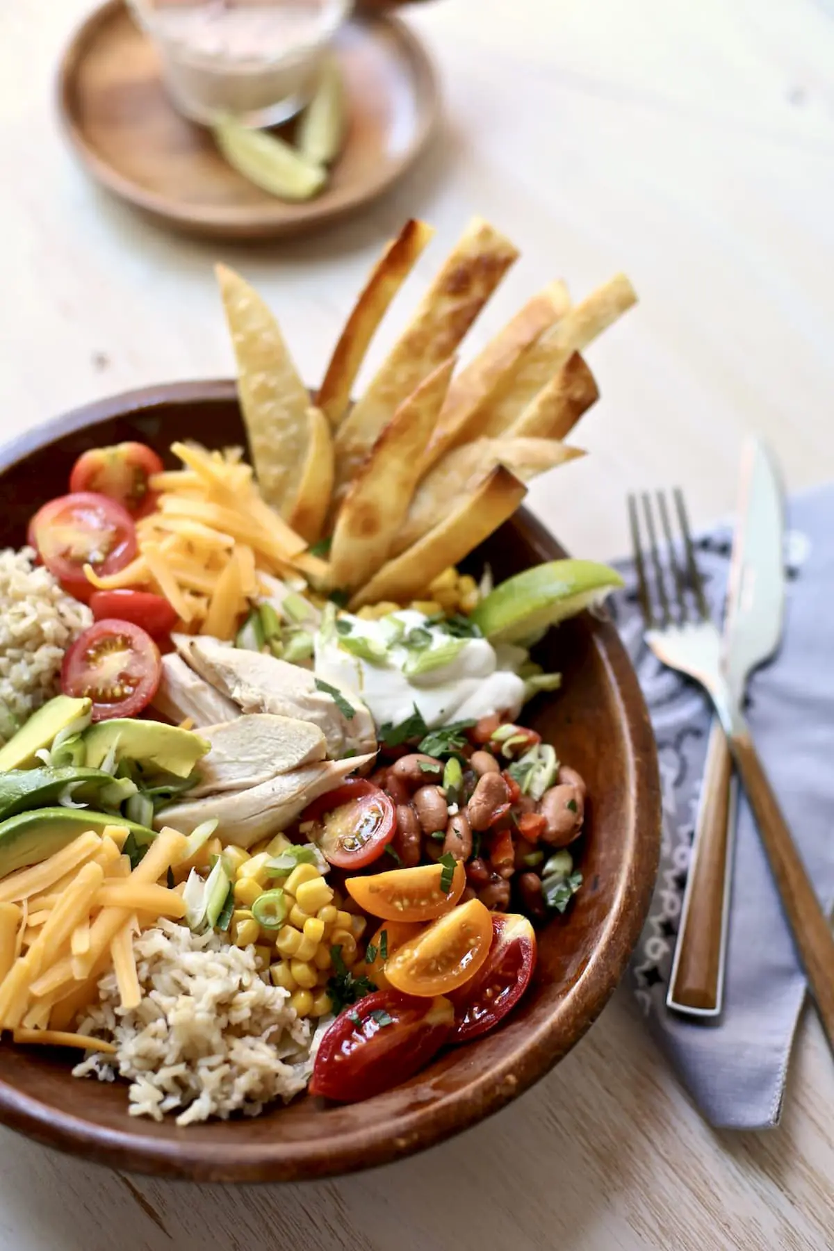 a bowl of beans rice tomatoes avocado tortillia cheese and corn in a wooden bowl