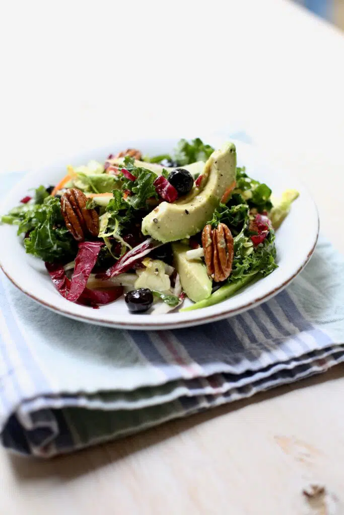 tossed green salad on a white plate on top of a striped cloth.