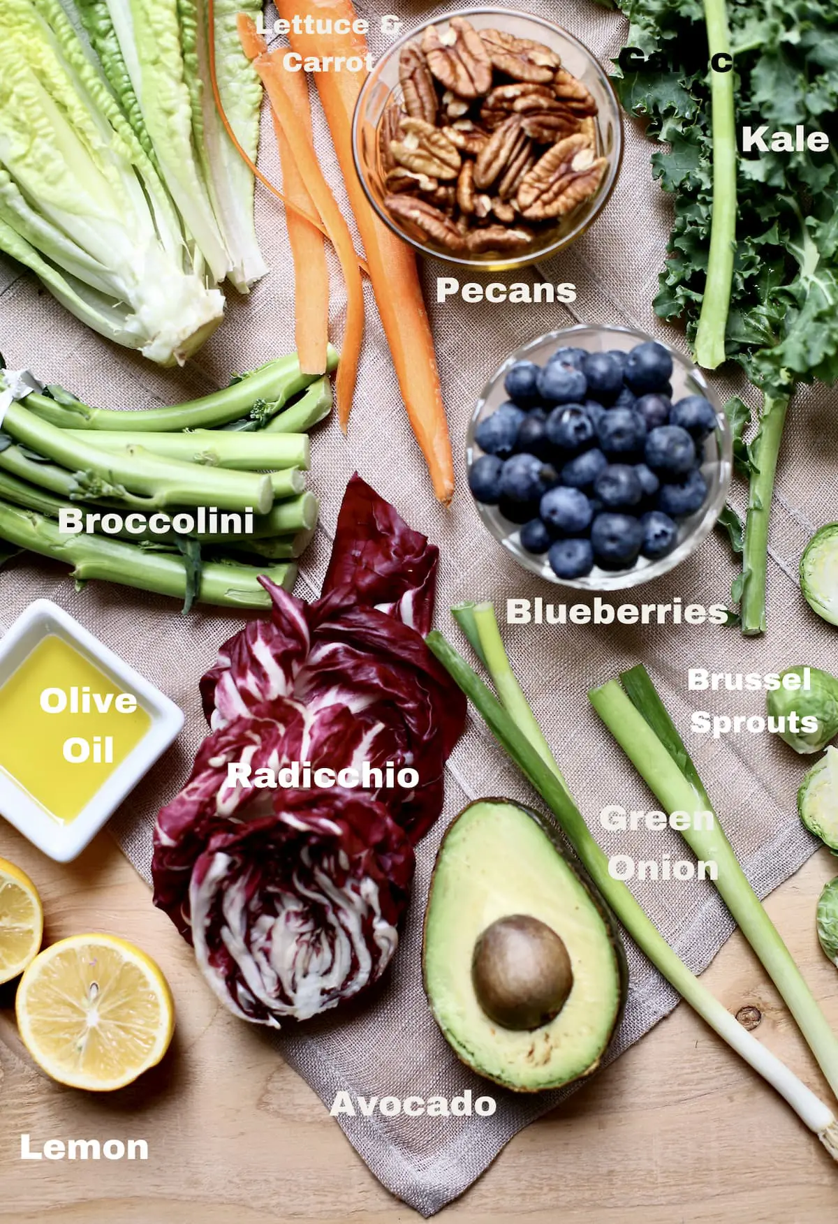 vegetables on a table with text overlay saying what they are: blueberries, brocolini, olive oil, avocado, green onion, pecans and more. 