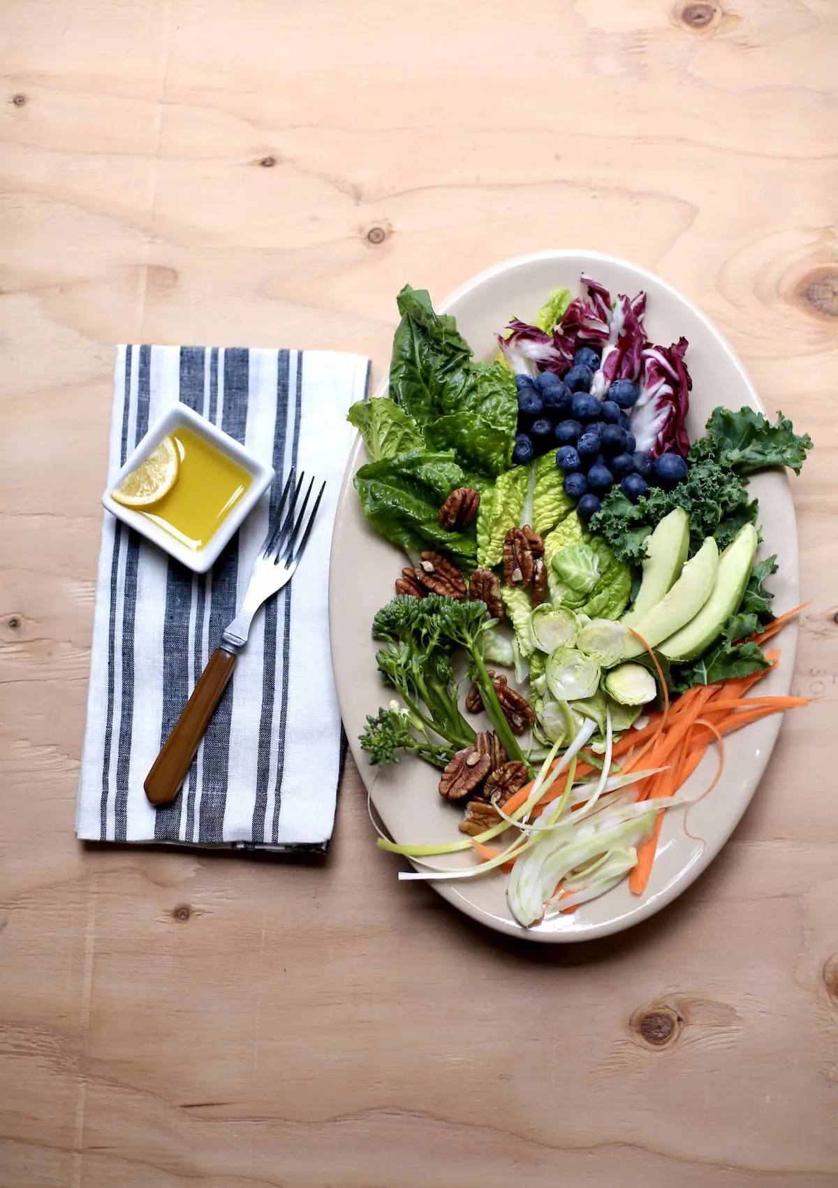 a large white platter of salad with a fork and lemon dressing alongside.