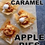 three little caramel apple pies on a gray table on parchment paper with ice cream and caramel sauce drizzled over the top