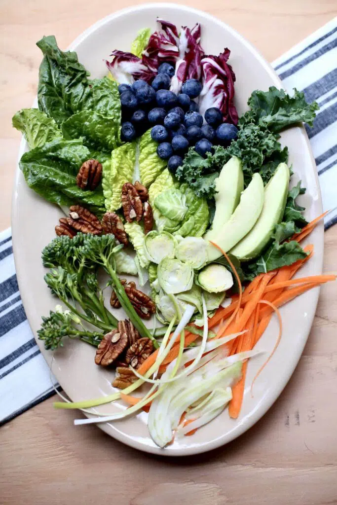 avocado, blueberries, greesn, carrot, fennel, pecans and more on a large white plate sitting on a table