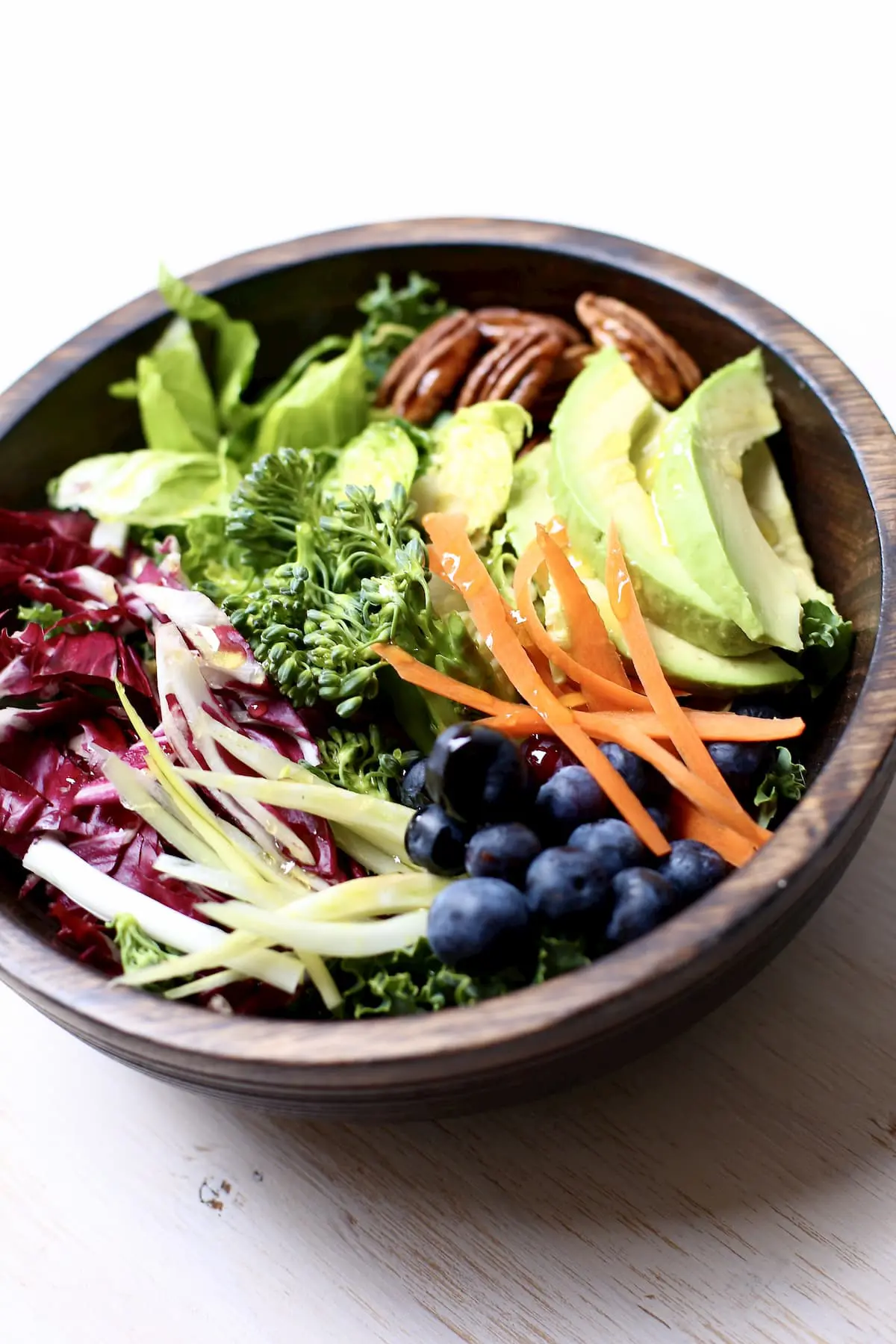 vegetables in a wooden bowl, greens, pecans, avocado, blueberries, pecans and carrots.