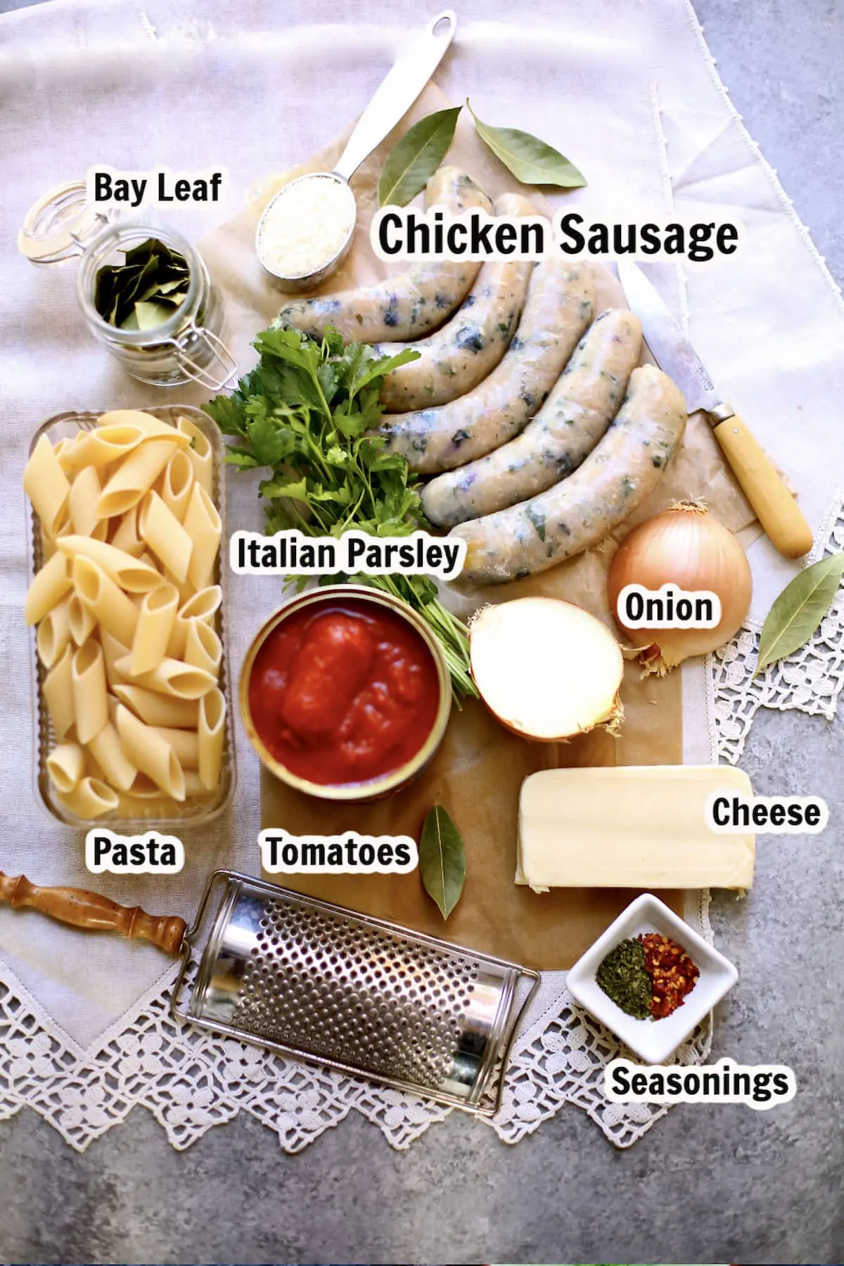 a table of ingredients for baked pasta with sausage, with text overlay saying what eash ingredient is. cheese, tomatos, sausage, pasta, seasonings.