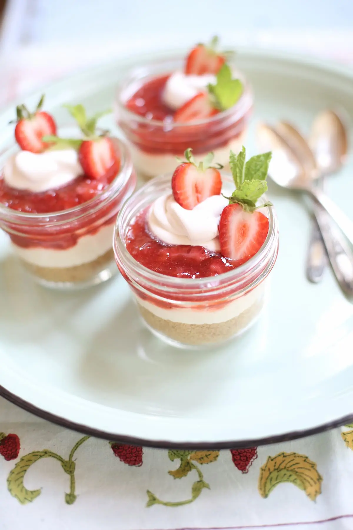 three jars of strawberry cheesecake desserts sitting on a blue tray with three spoons