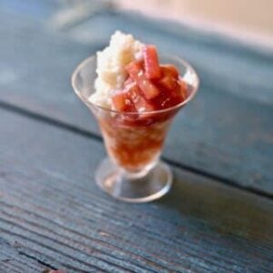 a small glass cup of rice pudding with rhubarb on a blue table