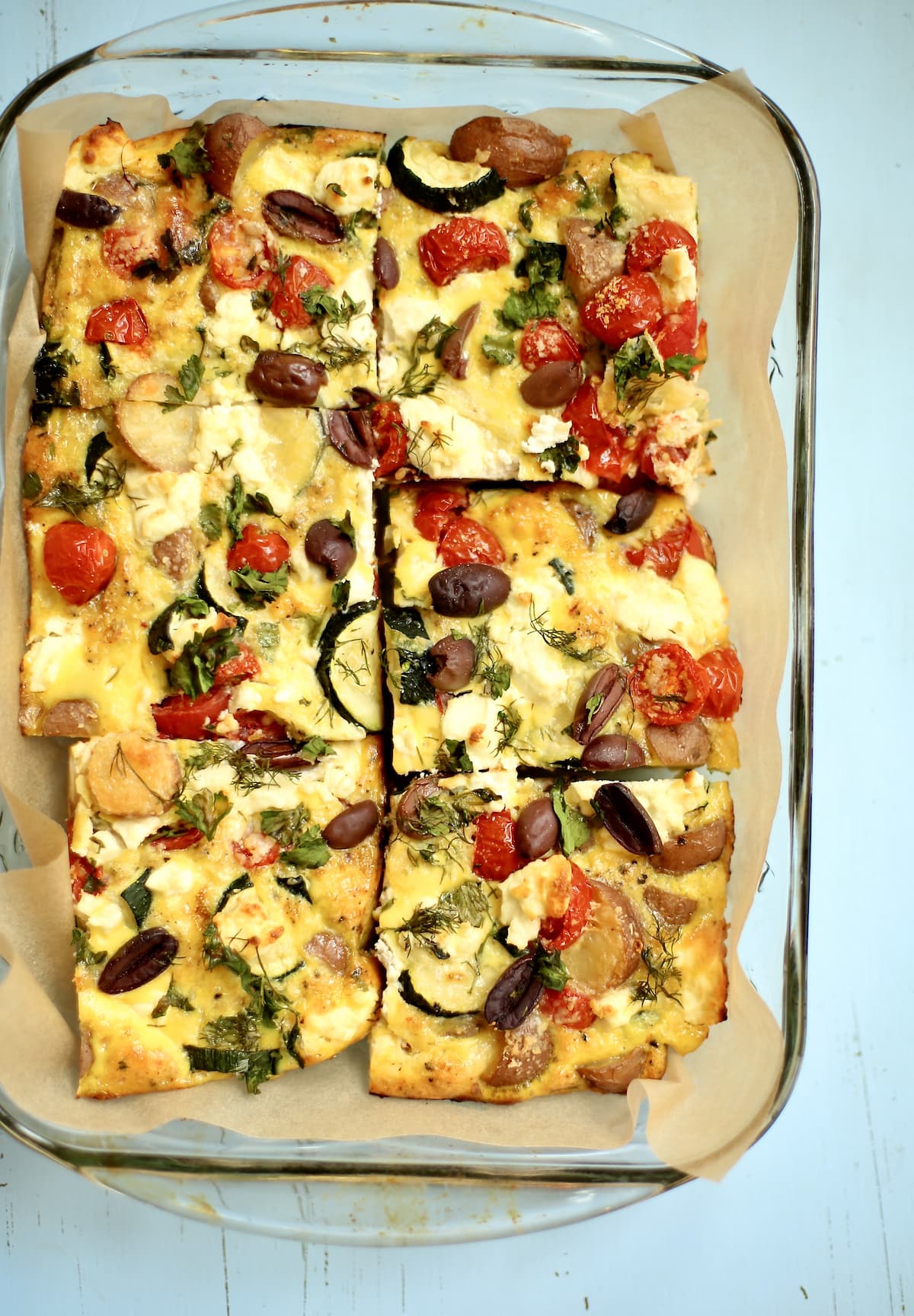 a cooked zucchini potato frittata thats been sliced in the baking pan into six pieces. 