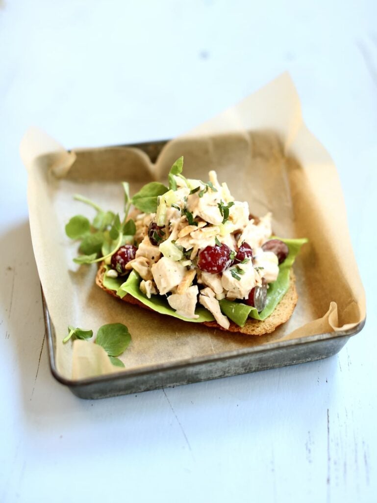 n open-faced chicken salad sandwich in a tin on a blue table