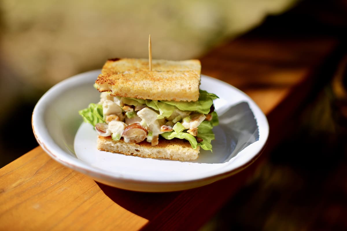 a chicken salad sandwich on a white plate outside