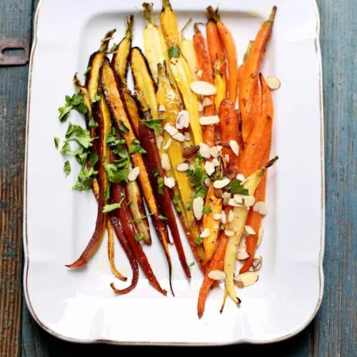 a finished tray of carrots with almonds on a platter and blue table.