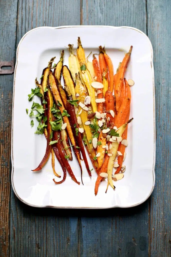 a finished tray of carrots with almonds on a platter and blue table.