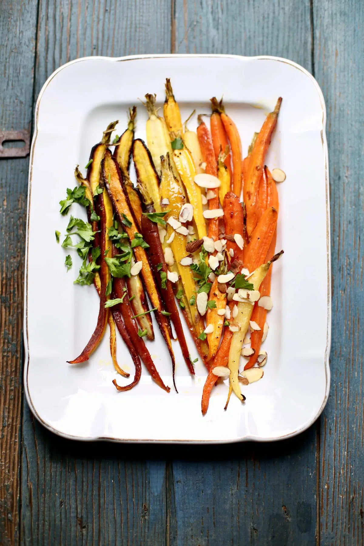 a finished tray of carrots with almonds on a platter and blue table.