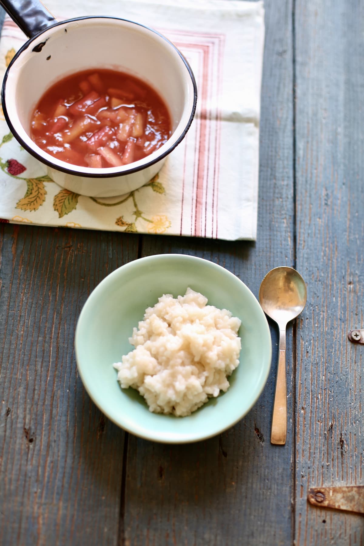 a bowl of rice pudding with a rhubarb sauce on the side on a blue table