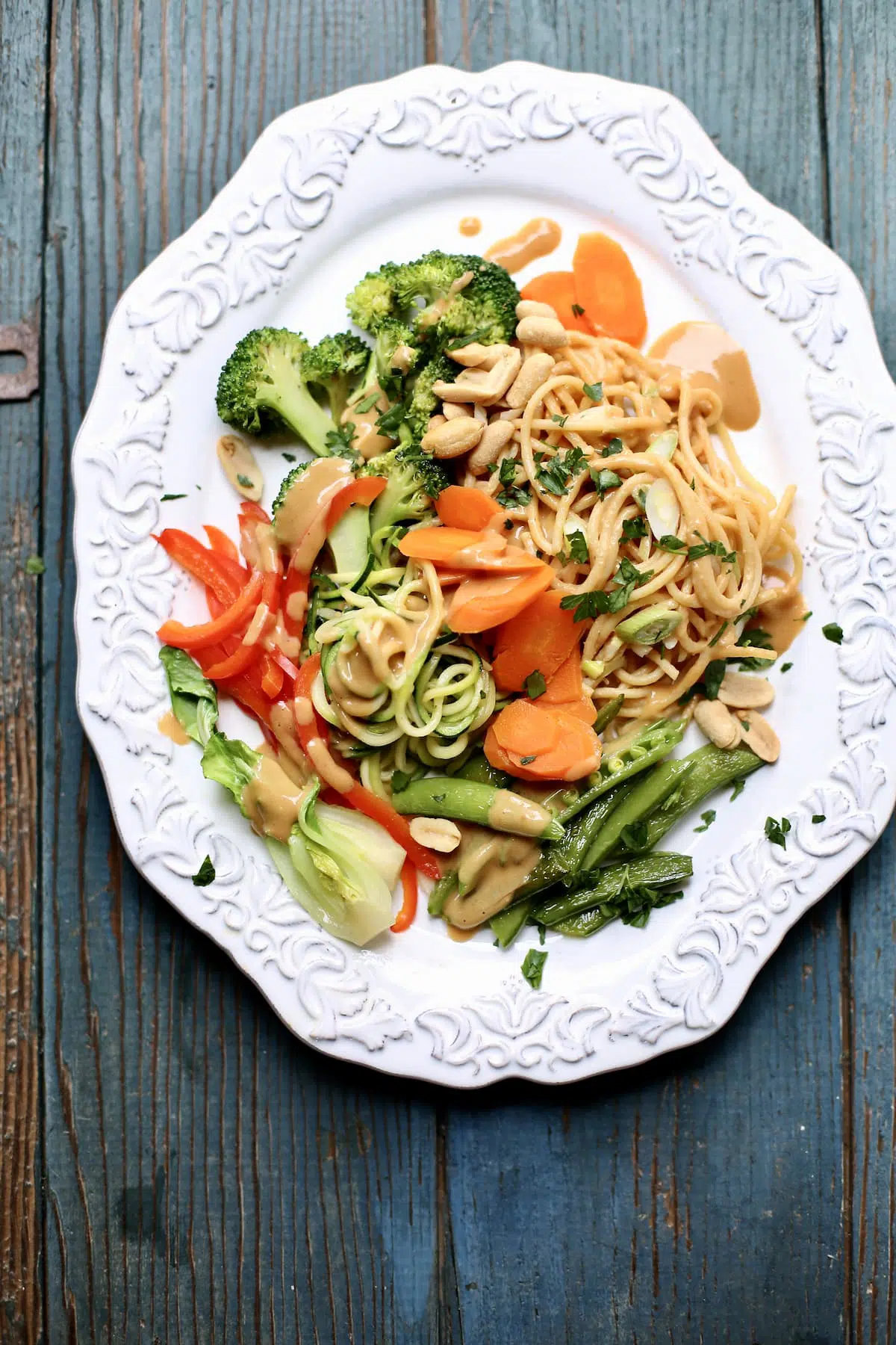 a cold noodle salad with peanut sauce and veggies on a white platter, sitting on a blue wooden table.
