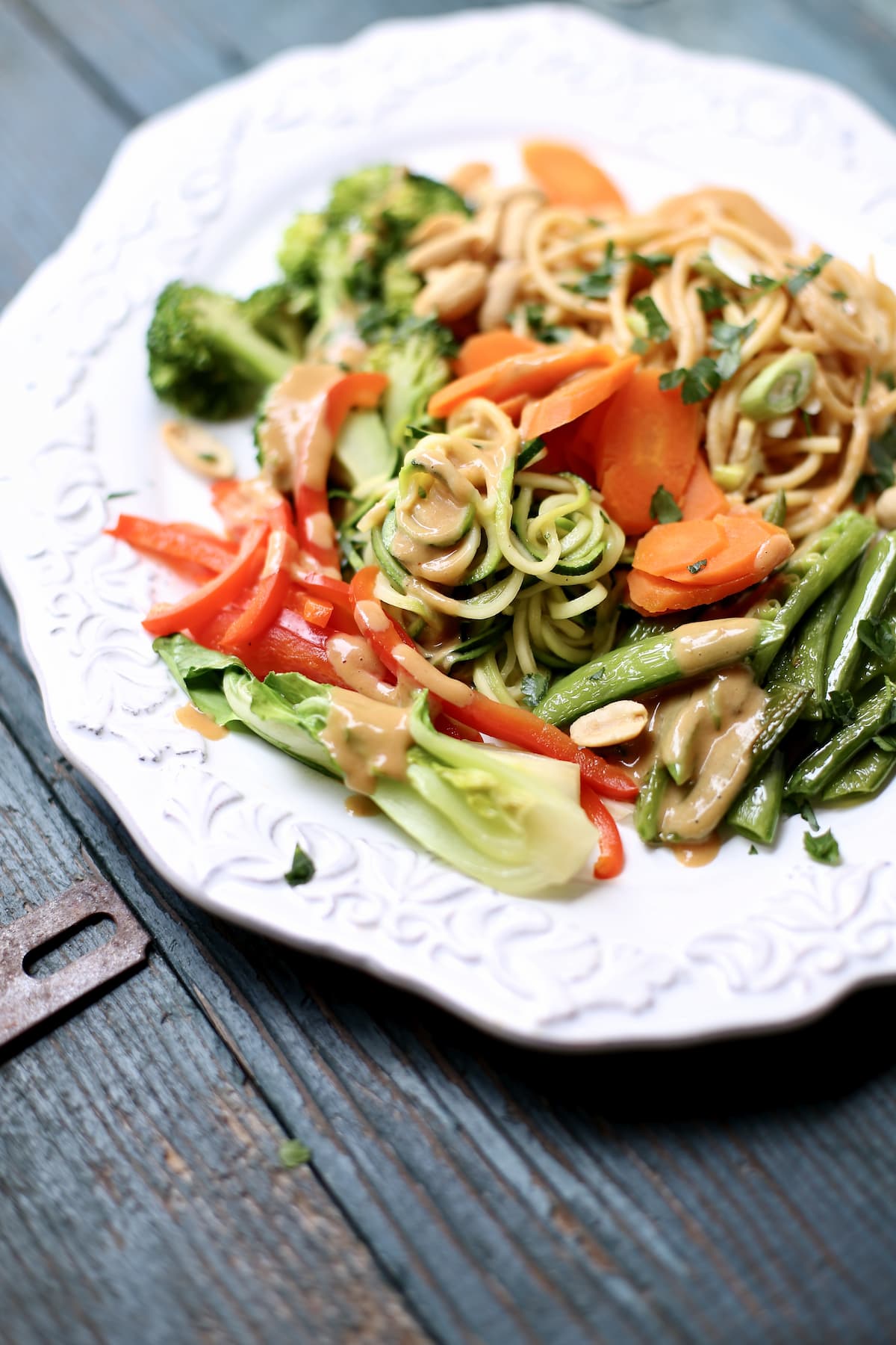 a white platter of noodle veggie peanut sauce salad on a blue table