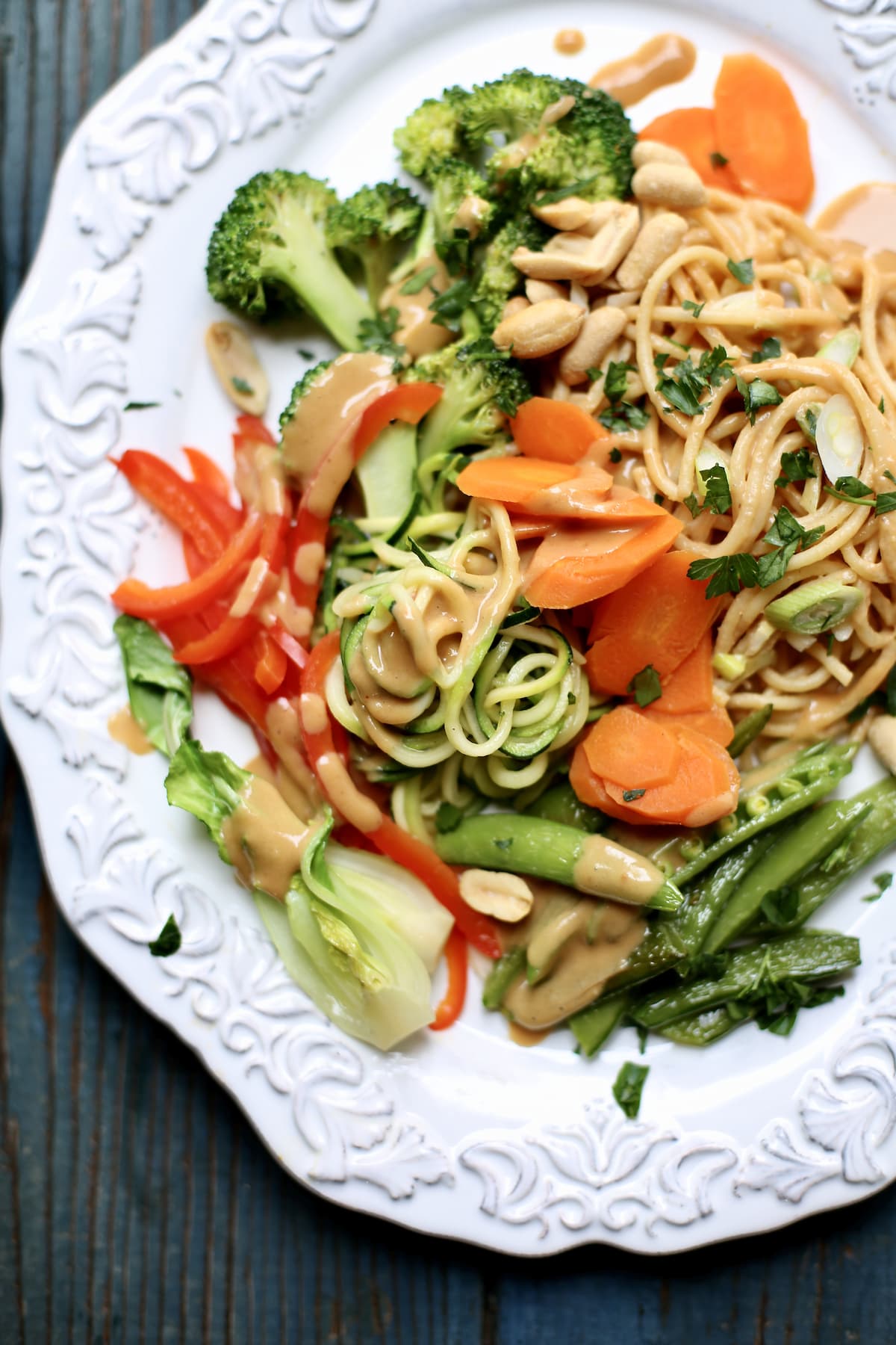 a white plate with different fresh vegeatbales and noodles and peanut sauce