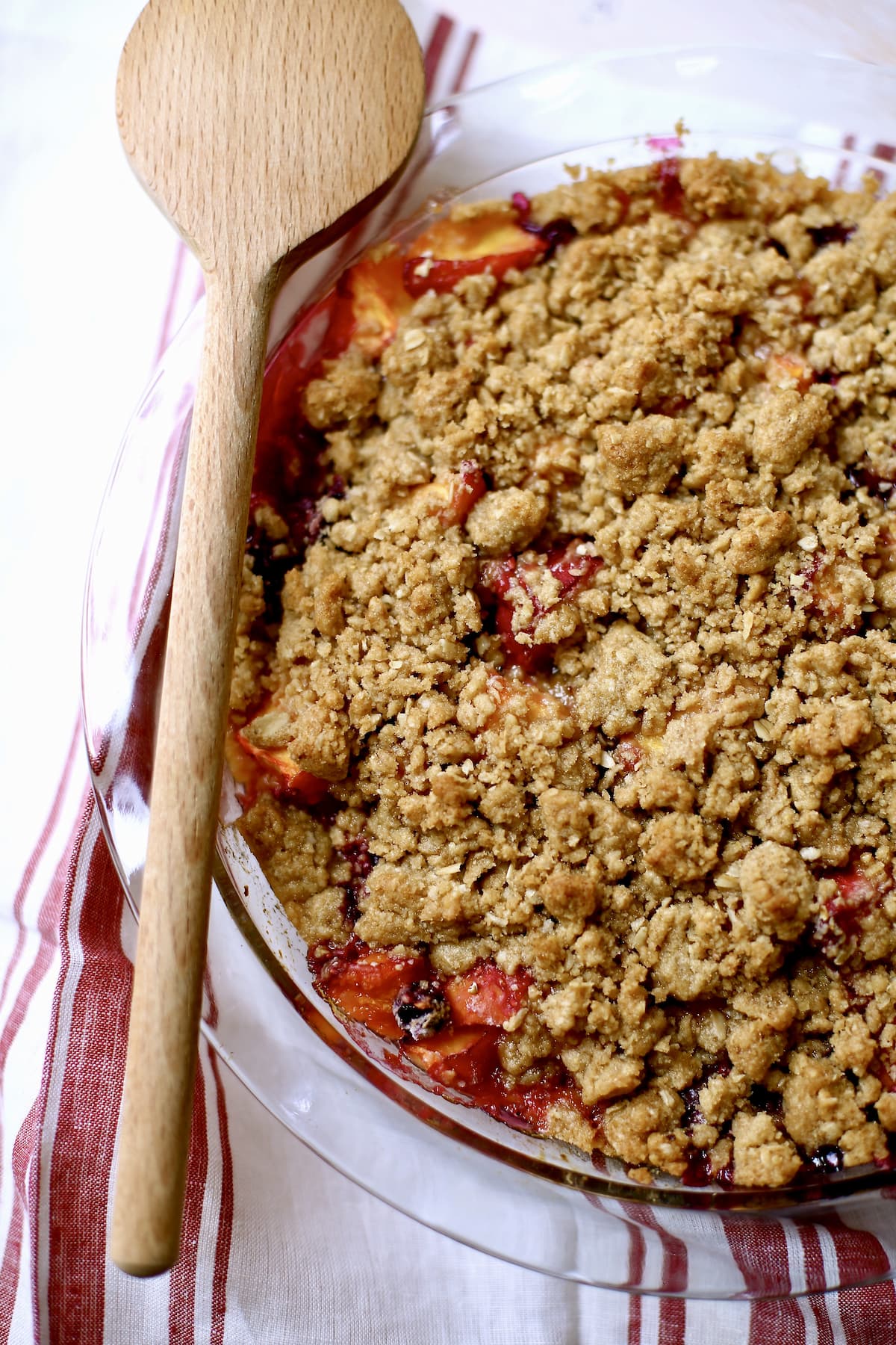 a fruit crisp with a wooden spoon next to it on a striped towel.