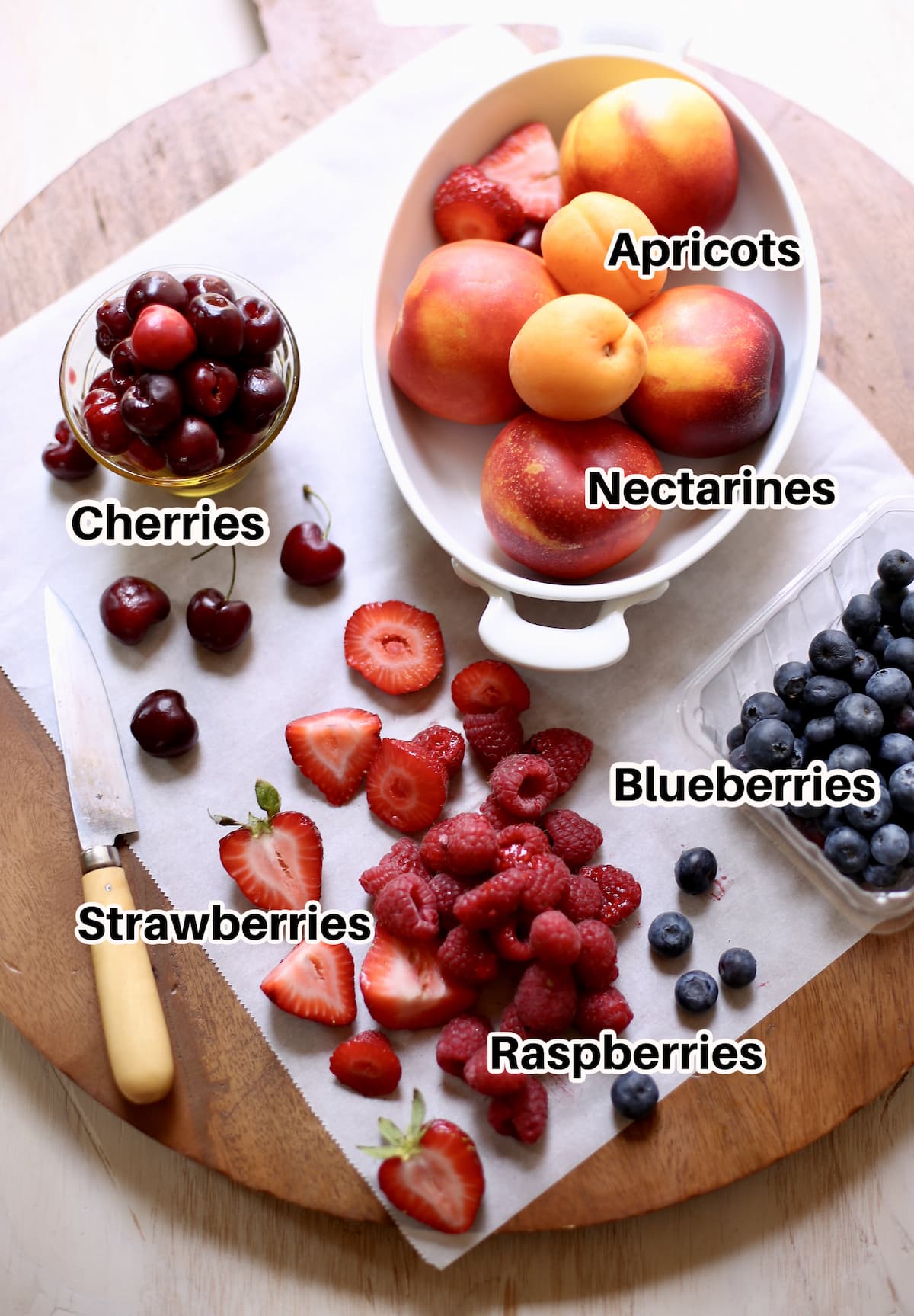 A tableful of fresh fruit, nectarines, raspberries, bluberries, strawberries, cherries. A knife sits nearby.