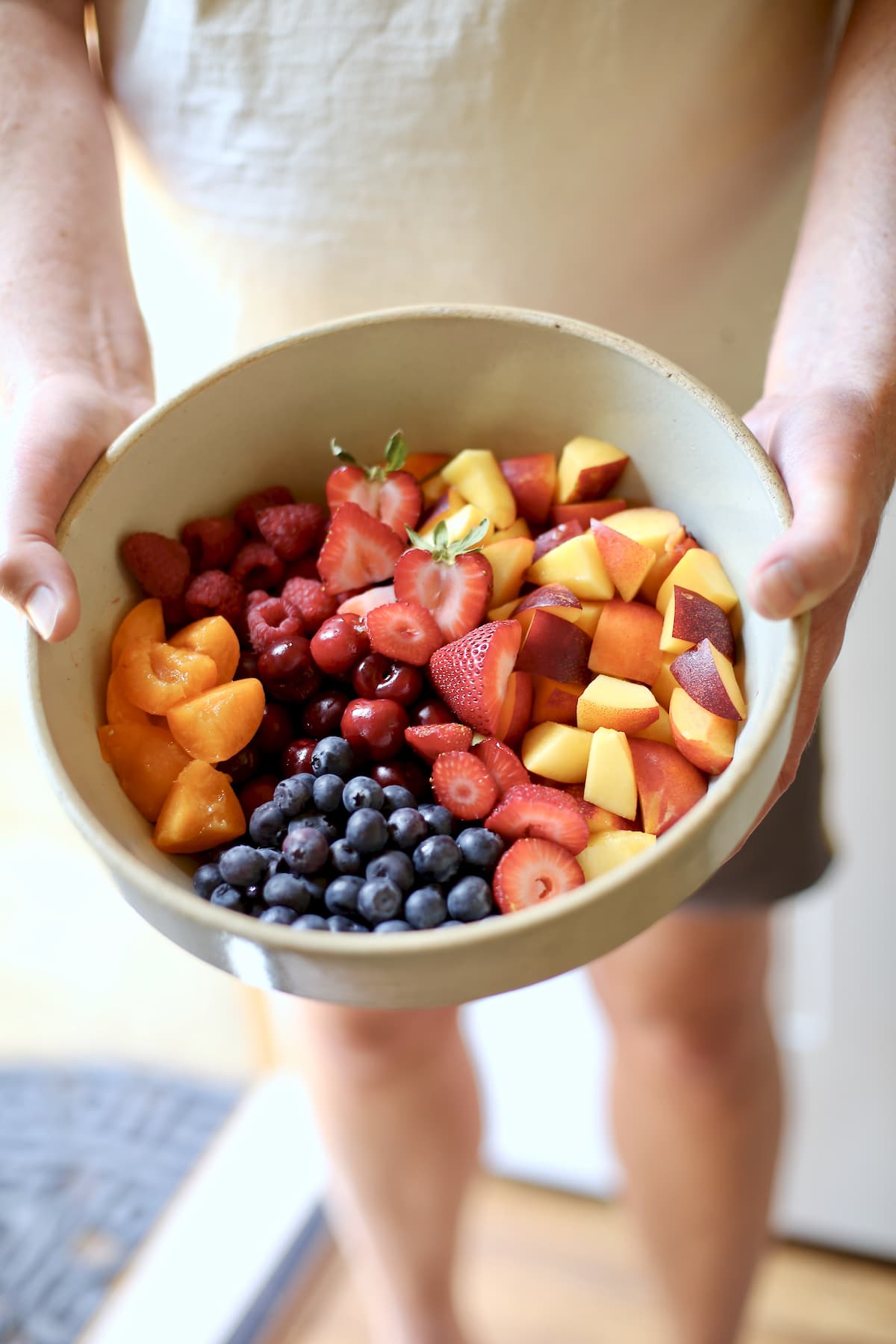 a bowl of fresh fruit held by a person with shorts on.