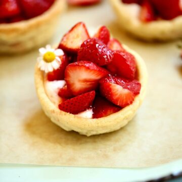 a small fresh strawberry pie in a cookie cup with whipped cream sitting on a serving tray.
