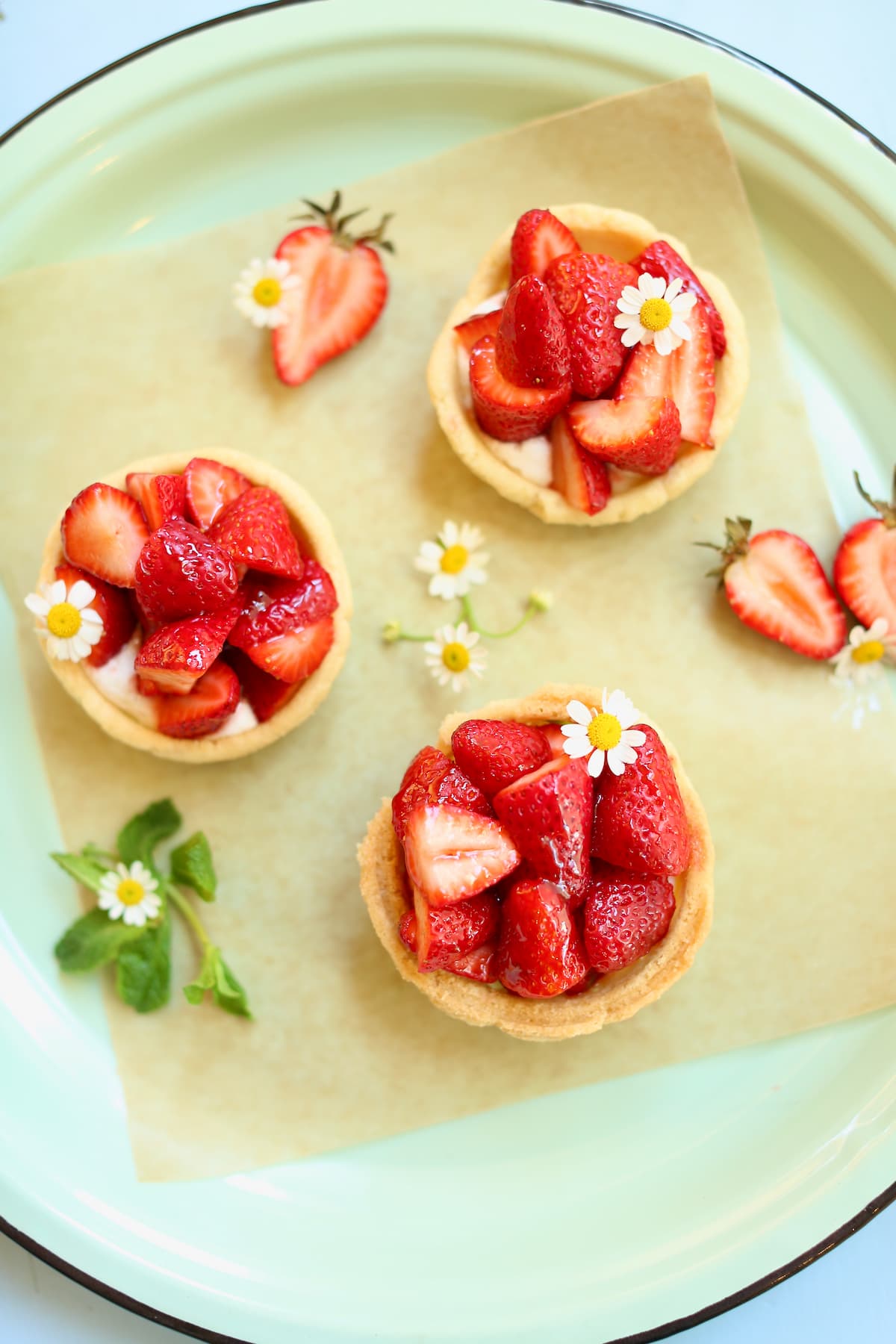 three small strawberry pies on a serving platter with fresh mint and small white flowers as garnish.