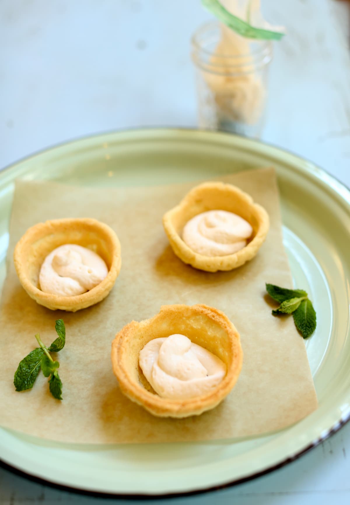 three cookie cups with whipped cream inside on a green serving tray with fresh mint on the side. 