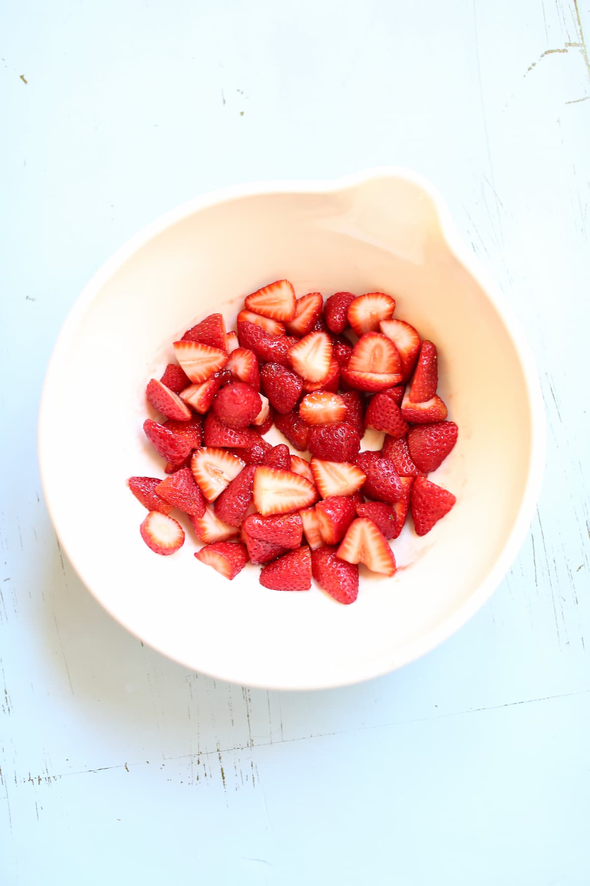 a white bowl of freshly sliced strawberries on a light blue table.