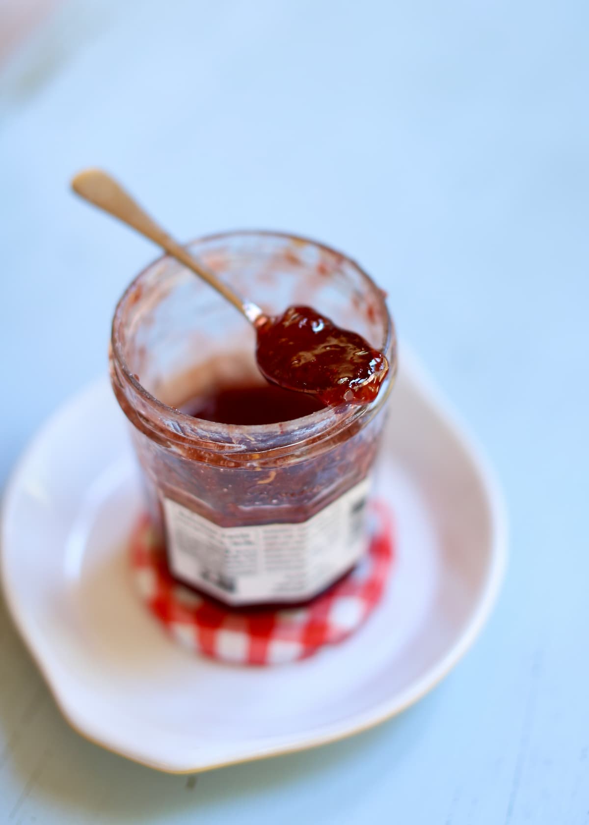 a jar of strawberry jam with a spoon coming out of it on a white b=plate sitting on a blue table