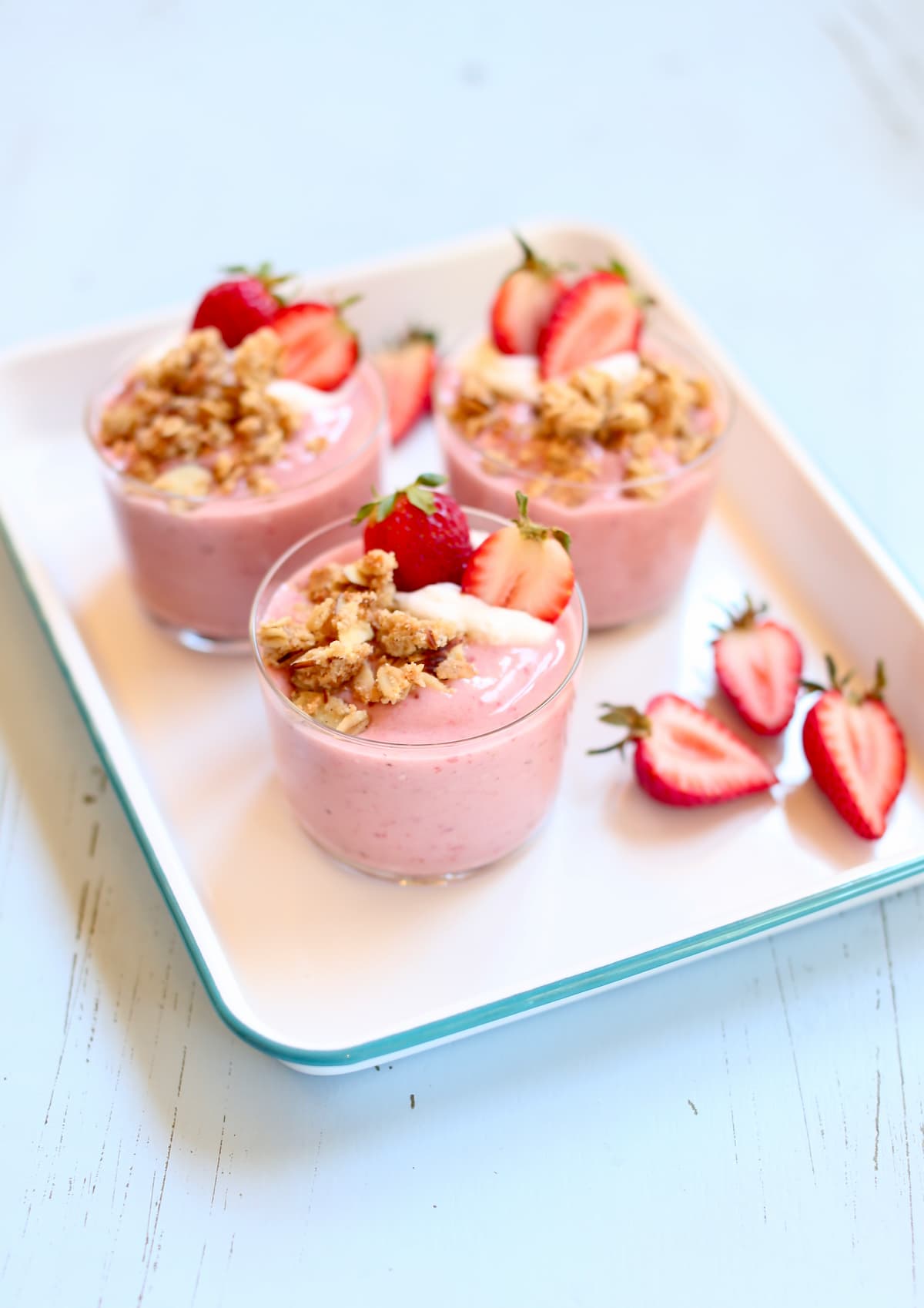 a whote tray holding several strawberry smoothies with fresh strawberry garnish on the side.