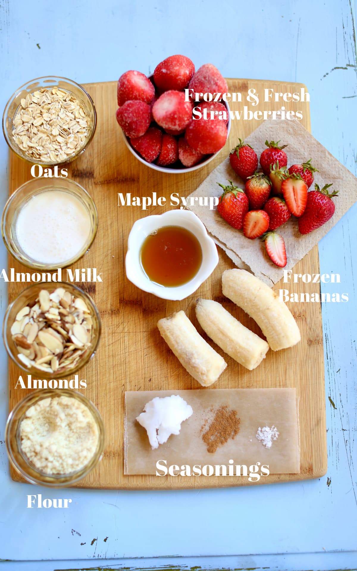 ingredients for a smoothies, bananas, maple syrup, strawberries fresh and frozen. almond milk, almonds, oatmeal.
